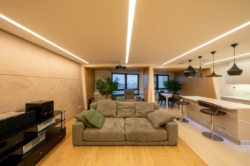 Big, gray sofa standing on beige wooden floor of a bright, luxurious living room interior